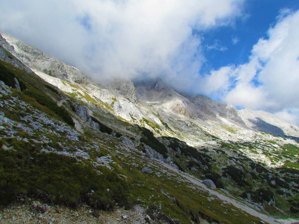 Живописный вид на залитый солнцем альпийский ландшафт в Триглавском национальном парке и Юлианские Альпы в Горенской области Словении с горными вершинами, окутанными облаками - Фото, изображение