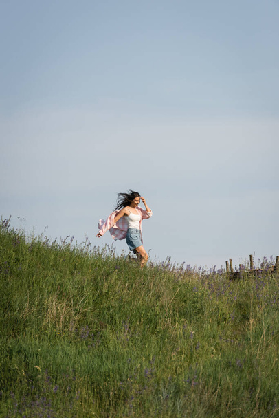 excited woman running in grassy field with wildflowers on summer day - Photo, image