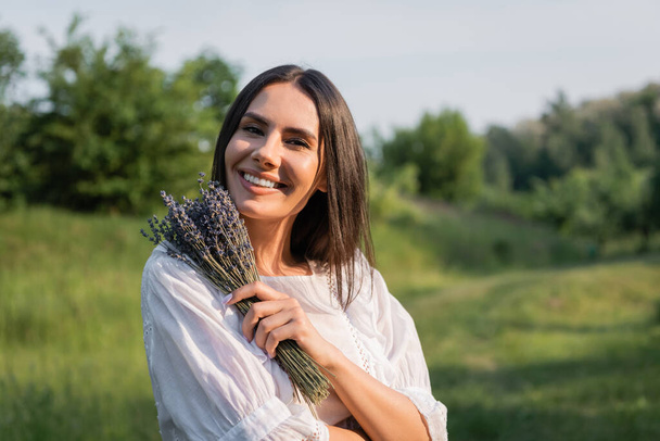 happy brunette woman with bouquet of lavender looking at camera outdoors - Foto, imagen