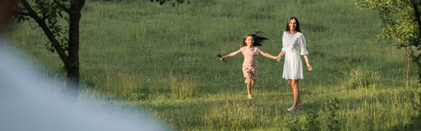 excited girl holding hands with mother while walking in field, banner - Photo, Image