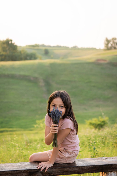 positiivinen tyttö peittää kasvot laventeli kimppu ja katsot kameraa maaseudulla - Valokuva, kuva