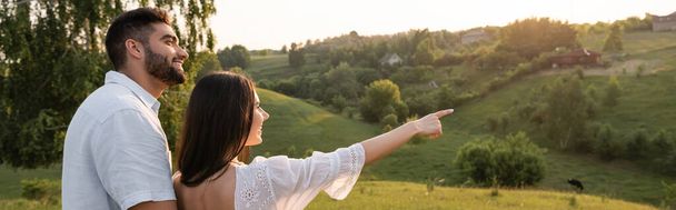 smiling woman pointing at picturesque hills near happy man in countryside, banner - Foto, Bild