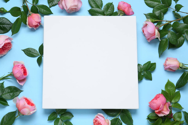 Blank canvas and beautiful pink roses on light blue background, flat lay. Space for design - 写真・画像
