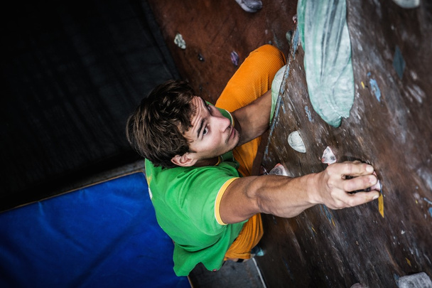 Uomo muscolare che pratica l'arrampicata su una parete rocciosa al chiuso  - Foto, immagini