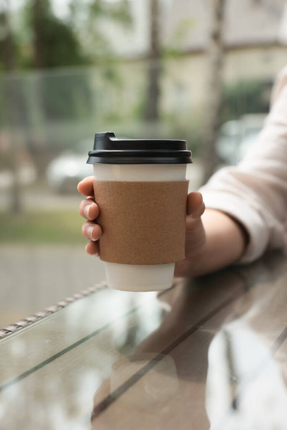 Woman holding paper takeaway cup at glass table outdoors, closeup. Coffee to go - Foto, afbeelding