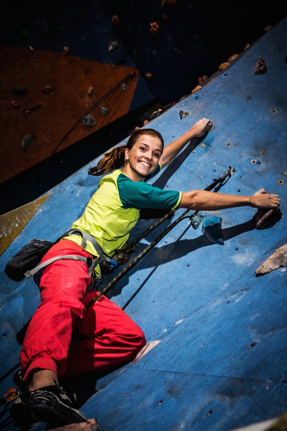 Mujer joven practicando escalada en roca en una pared de roca en el interior
 - Foto, Imagen