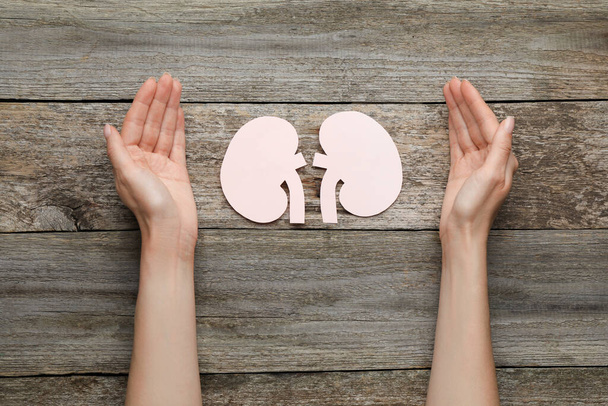 Woman protecting paper cutout of kidneys at wooden table, top view - Foto, afbeelding
