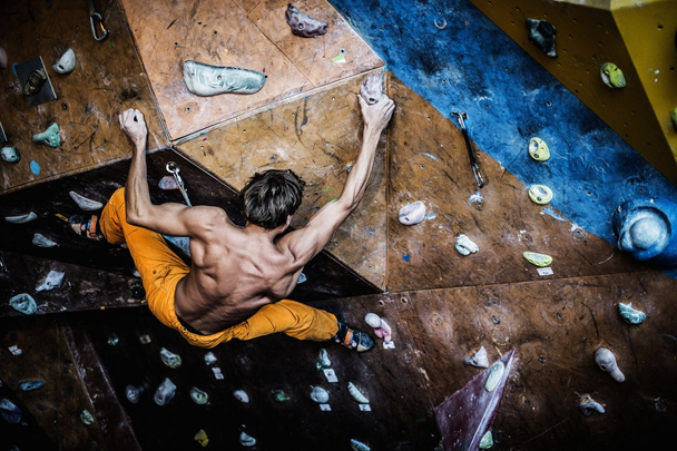 Uomo muscolare che pratica l'arrampicata su una parete rocciosa al chiuso  - Foto, immagini