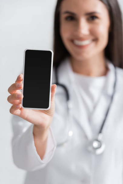 Blurred doctor in white coat holding cellphone with blank screen in clinic  - Photo, Image