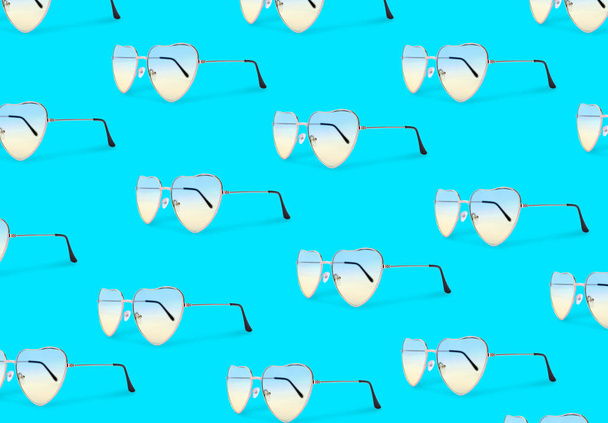 Many stylish heart shaped sunglasses on turquoise background. Seamless pattern design - Photo, Image