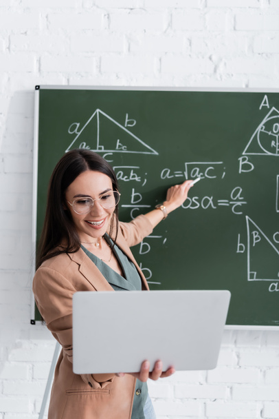 Teacher pointing at math formulas on chalkboard during online lesson in class  - Foto, Imagen