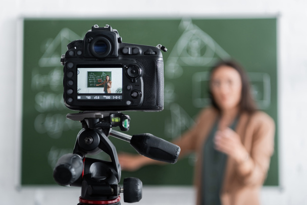 Θολή δάσκαλος στέκεται κοντά σε μαυροπίνακα και ψηφιακή φωτογραφική μηχανή  - Φωτογραφία, εικόνα