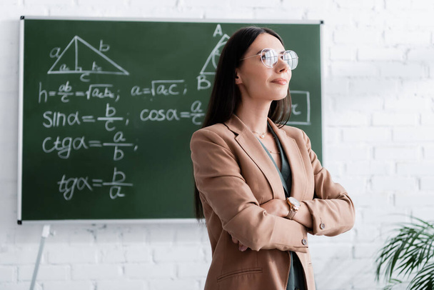Teacher in eyeglasses standing near chalkboard in school   - Фото, зображення
