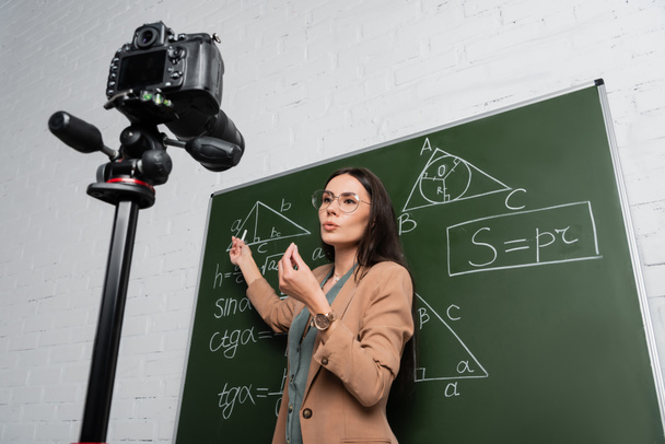 Low angle view of teacher talking near math formulas on chalkboard and digital camera in school  - Foto, immagini