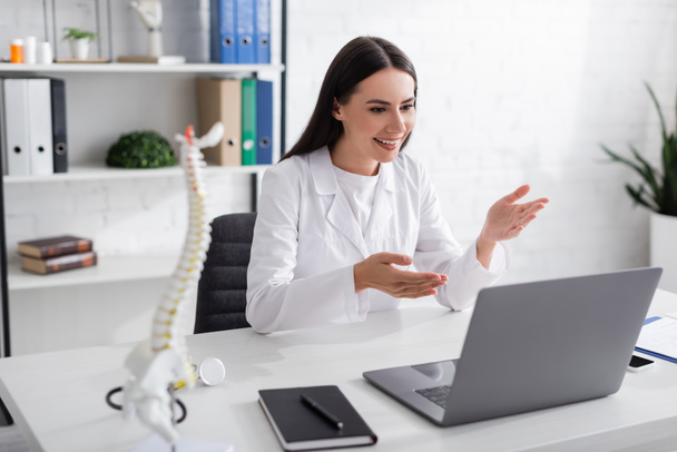 Smiling doctor pointing at laptop during online consultation in hospital   - Foto, Imagem