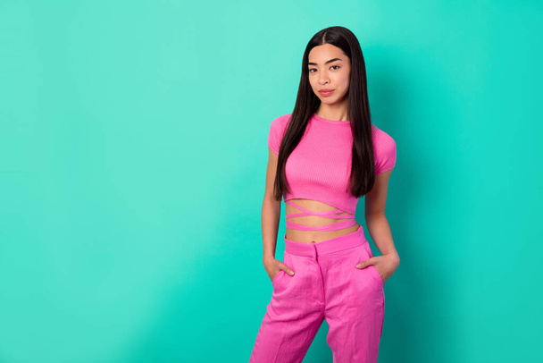 Photo of stunning young female hold hands in pockets wear stylish crop top crossed over belly isolated on teal color background. - Foto, Imagem