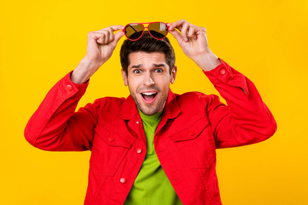 Photo of cool millennial brunet guy hold eyewear wear red shirt isolated on yellow color background. - Fotó, kép