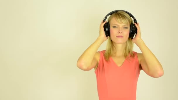 Young attractive woman listens to music with headphones - horrible music- studio - Metraje, vídeo