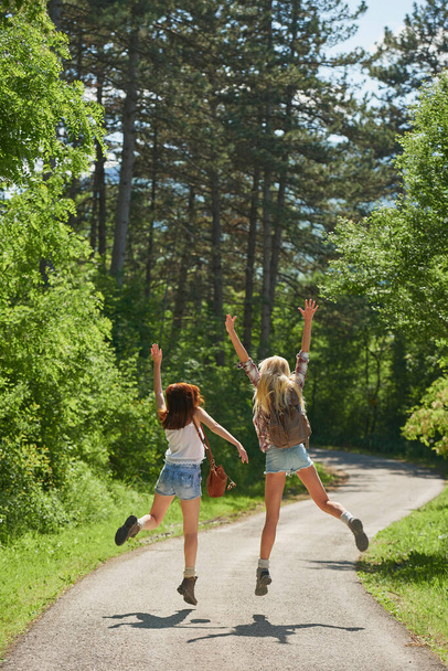 Dva veselí přátelé skáčou a slaví spolu na výletě do lesa. Dvě ženy vesele skákají a oslavují na prázdninovém výletě v odlehlém lese. - Fotografie, Obrázek
