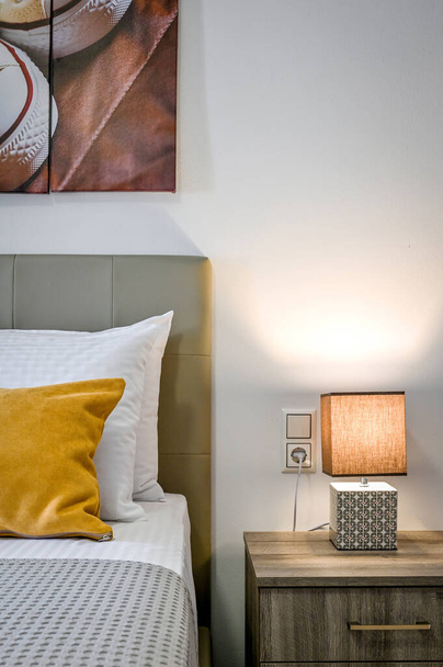 Bedroom interior details. Part of bed with pillows and bedside table with switched on lamp on it.  - Photo, image