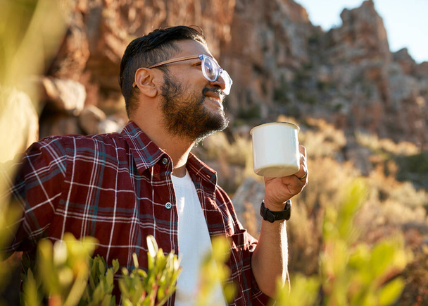 Un hombre del sur de Asia sonríe mientras bebe café en un viaje de campamento en las montañas. Foto de alta calidad - Foto, Imagen