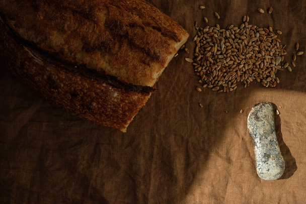 Stone-age knife, bread, and wheat on the linen tablecloth. Sun shadow. - Photo, Image