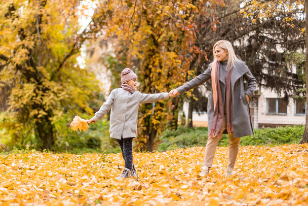 šťastná rodina matka a dcera dítě hrát a smát se na podzimní procházce. Vztahy mezi matkou a dítětem. Módní matka a dcera ve stylovém vzhledu se stejnými bundami. - Fotografie, Obrázek