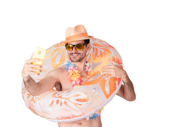Close-up portrait of a smiling young tourist wearing a flower necklace and hat and sunglasses and wearing an inflatable float posing for a selfie photo. - 写真・画像