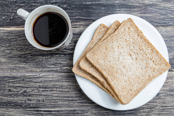 Sliced bread on the plate and a cup of coffee on the wooden background - Fotoğraf, Görsel