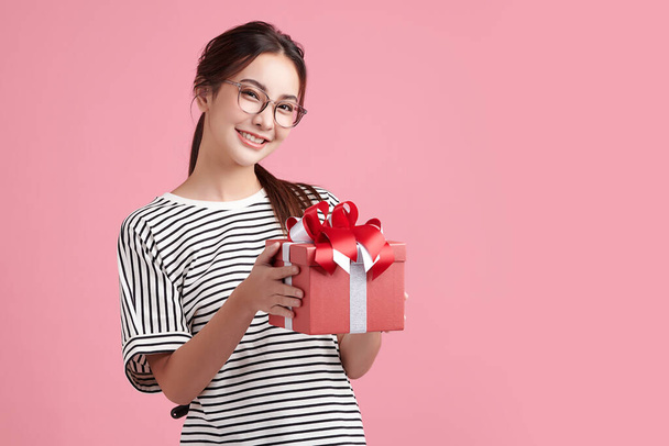 Симпатичная азиатка держит подарочную коробку и стоя на розовом фоне, пустое место для копирования вашего рекламного контента. - Фото, изображение