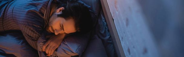 Κάτοψη του ανθρώπου στην πιτζάμα ξαπλωμένος στο κρεβάτι το βράδυ, πανό  - Φωτογραφία, εικόνα