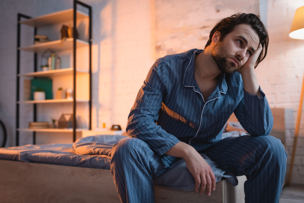 Tired man in pajama sitting on bed at night  - Zdjęcie, obraz