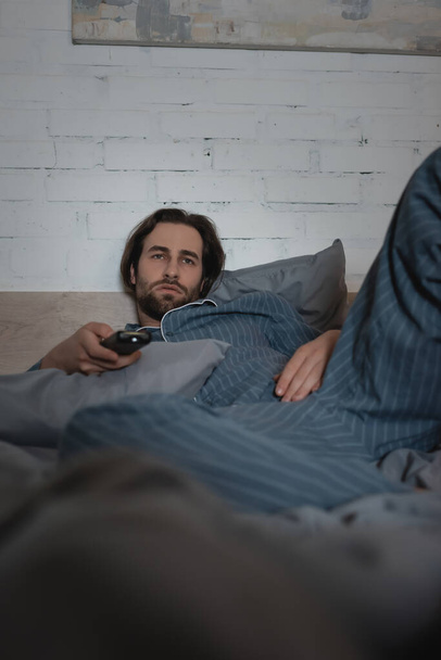 Bearded man in pajamas watching tv on bed at night  - Fotoğraf, Görsel