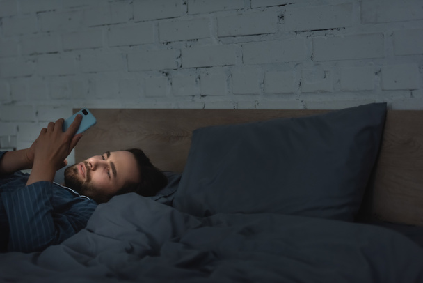 Young man using smartphone on bed at night  - Foto, Imagen