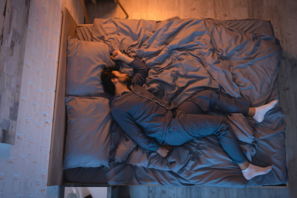 Top view of man in socks and pajama sleeping on bed at night  - Valokuva, kuva