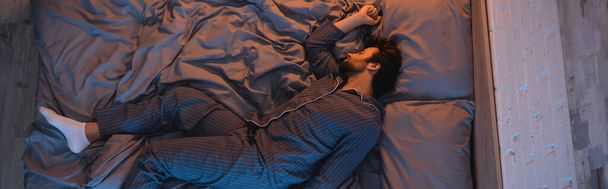 Vista superior del hombre en pijama durmiendo en el dormitorio por la noche, pancarta  - Foto, imagen