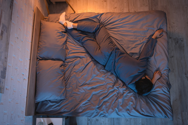 Side view of man in pajama and socks sleeping in bedroom  - 写真・画像
