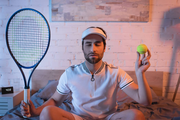 Sleepwalker with closed eyes holding tennis rocket and ball on bed  - Foto, immagini