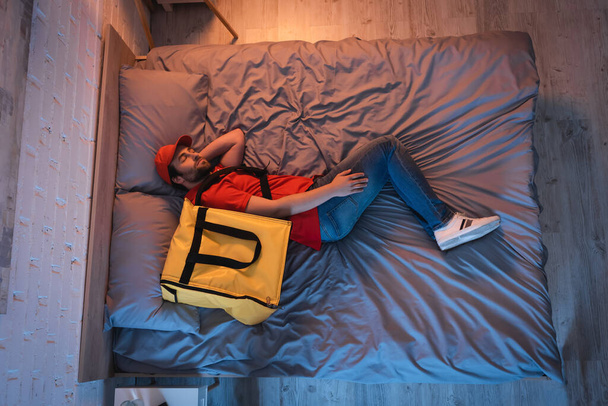 Top view of sleepwalker in delivery uniform sleeping on bed at night  - Fotó, kép