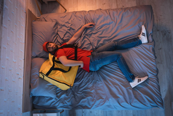Vue du dessus du somnambule en uniforme de livraison dormant sur le lit à la maison  - Photo, image