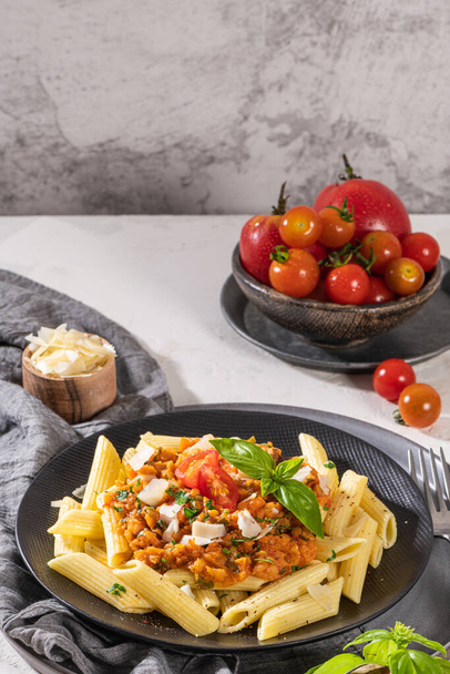 Tasty appetizing classic italian penne pasta with vegetarian lentil bolognese sauce, cheese parmesan and basil on plate on light table. Healthy eating concept. - Photo, image