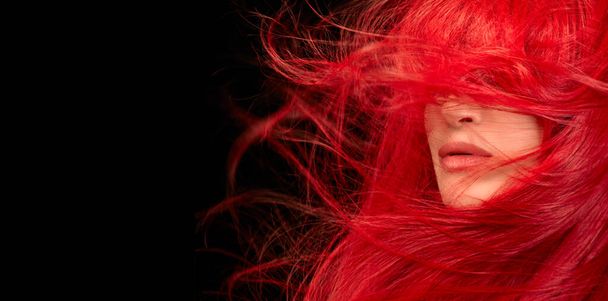 Βαμμένα μαλλιά φροντίδα και μόδα έννοια. Μόδα μοντέλο κορίτσι με ανεμοδαρμένα μακριά βαμμένα κόκκινα μαλλιά. Όμορφη κοκκινομάλλα με λαμπερά μακριά μαλλιά. Απομονωμένα σε μαύρο με αντιγραφικό χώρο - Φωτογραφία, εικόνα