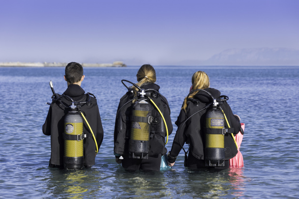 Scuba divers walking into the sea on a shore dive from behind - Foto, Imagen