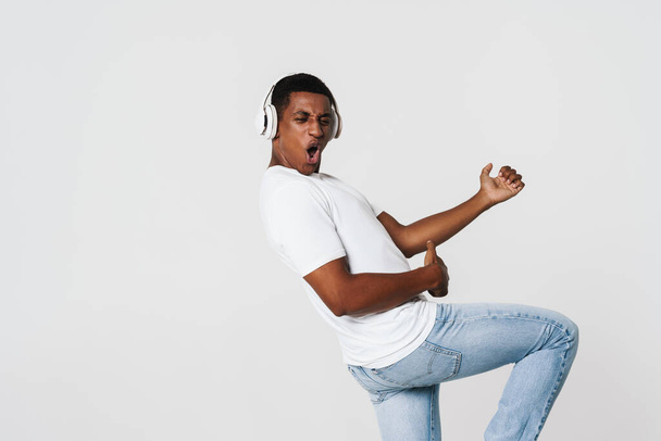 Young black man dancing while listening music with headphones isolated over white wall - Foto, Imagen