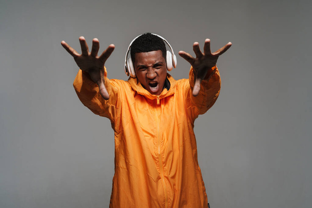 Young black man screaming and stretching his hands at camera isolated over grey wall - Foto, afbeelding