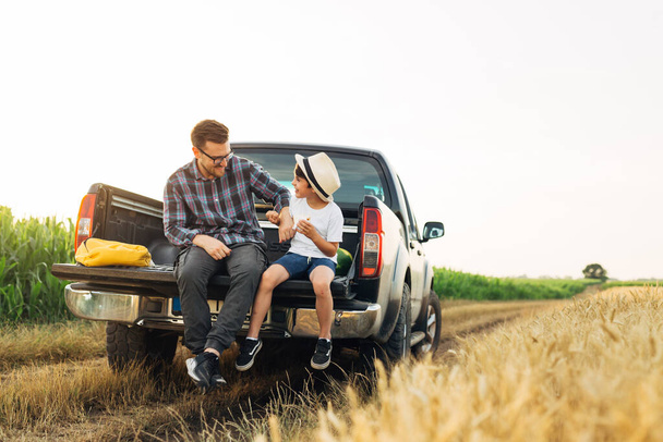 father and son sits on truck trunk outdoor on field . they enjoying time together - Фото, изображение