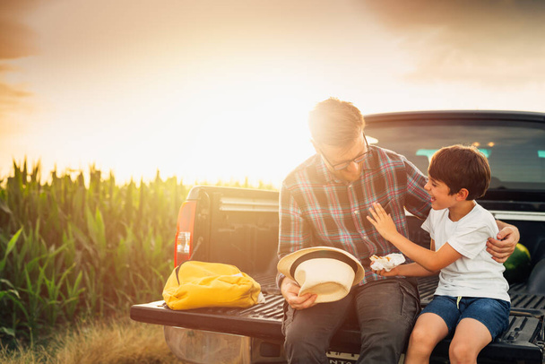 father and son sits on truck trunk outdoor on field . they enjoying time together - Fotografie, Obrázek