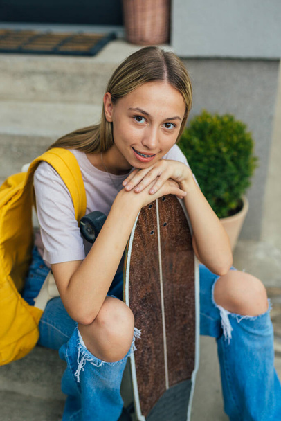 teenager caucasian girl sitting on front stairs at home and holding her skateboard - 写真・画像