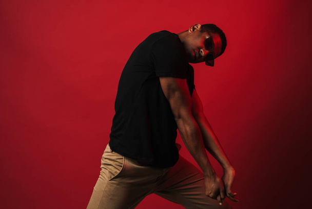 Young black man wearing sunglasses posing and looking at camera isolated over red wall - Фото, зображення