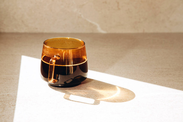 Black coffee in a transparent orange cup on a beige light background. Front view - 写真・画像